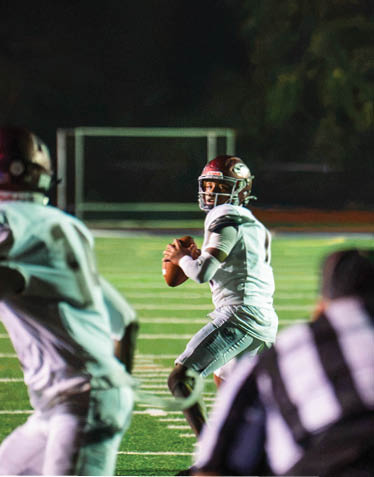 Two people in football uniforms are on a field at night, with one holding a football and preparing to throw it. Description generated by AI