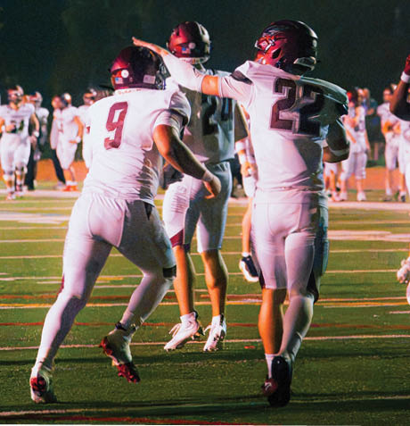 Several people wearing football uniforms are on a field at night, with one person in the center preparing to throw a football. Description generated by AI
