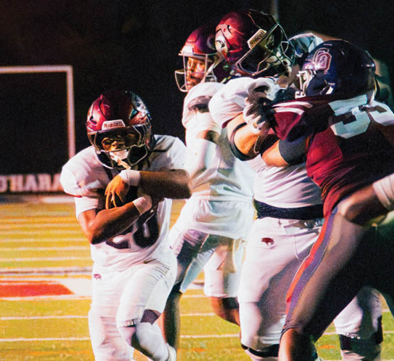 People in football uniforms are actively playing on a lit field during a nighttime game. Description generated by AI