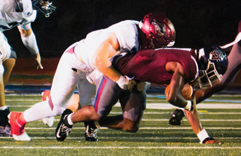 Two people in football uniforms are engaged in a tackle on a field under stadium lights. Description generated by AI