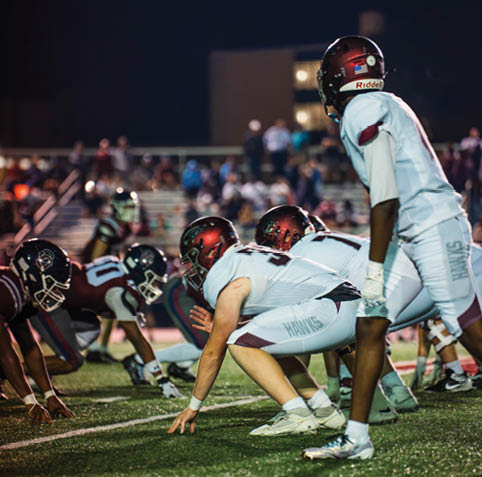 People in football uniforms are lined up on a field at night, preparing for a play during a game. Description generated by AI