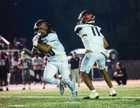 Two people wearing football helmets and uniforms are engaged in a game on a field at night. Description generated by AI