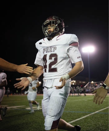 A person wearing a white football jersey with the number 42 and a maroon helmet is standing on a field at night with stadium lights in the background. Description generated by AI