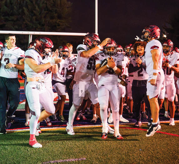 A group of people in football uniforms and helmets are celebrating energetically on a field at night. Description generated by AI