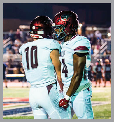 Two people wearing football helmets are facing each other closely against a dark night sky background. Description generated by AI