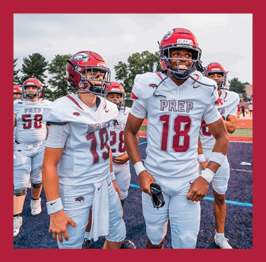 Two people wearing red football helmets are partially visible at the bottom of the image with a cloudy sky above them. Description generated by AI