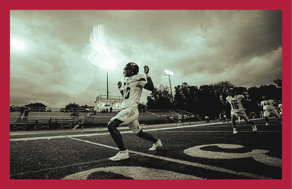 A person in a football uniform is preparing to throw a ball on a field under a cloudy sky with stadium lights and other players in the background. Description generated by AI