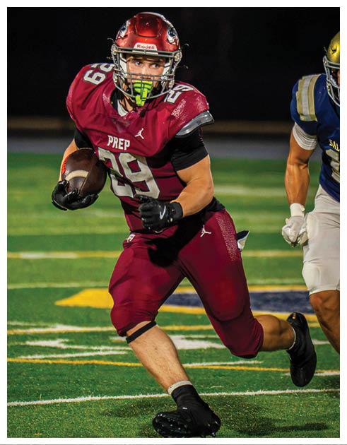 A person wearing maroon sports gear is running on a football field while holding a football. Description generated by AI