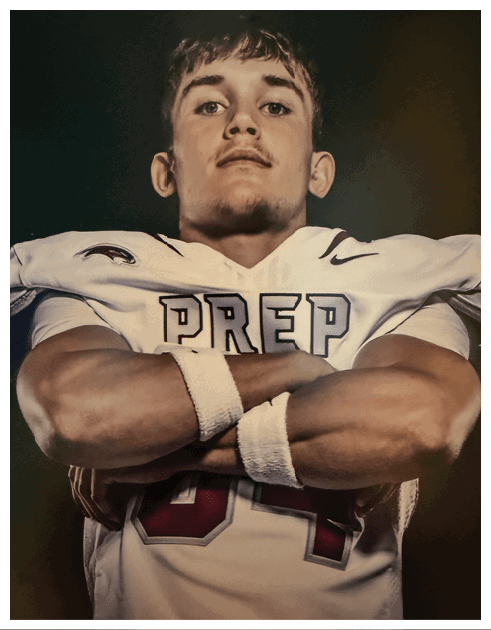 Person wearing a white sports jersey with the word “PREP" and crossed arms, standing against a dark background. Description generated by AI