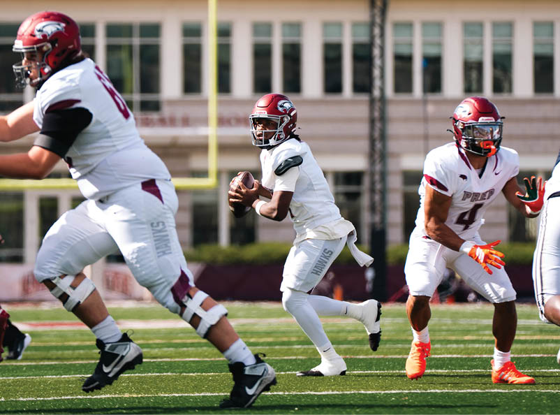 Three people in football uniforms are on a field with one person holding a football and preparing to pass while the others are in motion. Description generated by AI