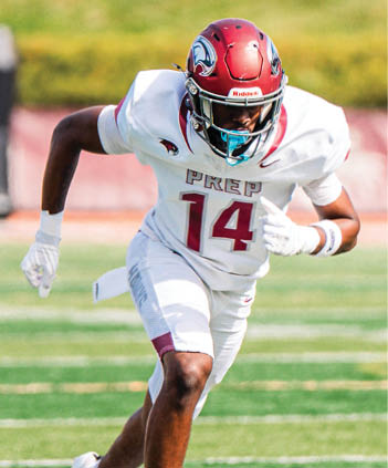 A person wearing a red helmet and white football uniform with the number 14 is running on a green football field. Description generated by AI