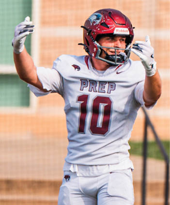 A person in a football uniform with the number 10 and a red helmet is standing on a field with arms raised near a goalpost. Description generated by AI