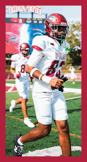 A person wearing a red helmet and white football uniform with the number 85 is walking on a football field with another player in the background. Description generated by AI