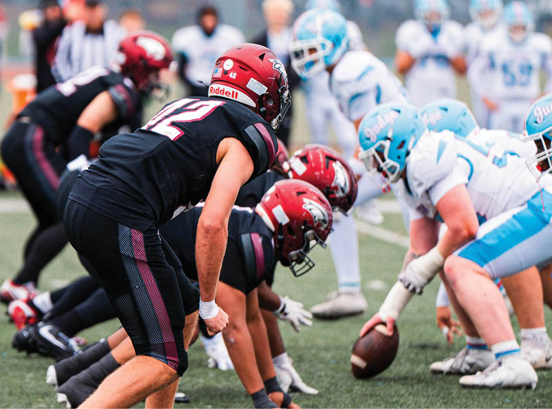 People in football uniforms are lined up on a field preparing for a play during a game. Description generated by AI