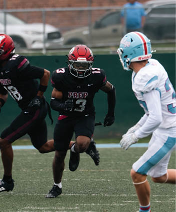 Two people in black football uniforms with “PREP" on the jerseys are running on a field during a game. Description generated by AI