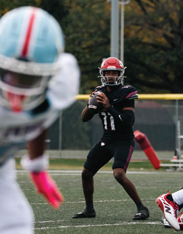 A person wearing a black sports uniform with the number 11 is holding a football in a ready-to-throw position on a grassy field. Description generated by AI