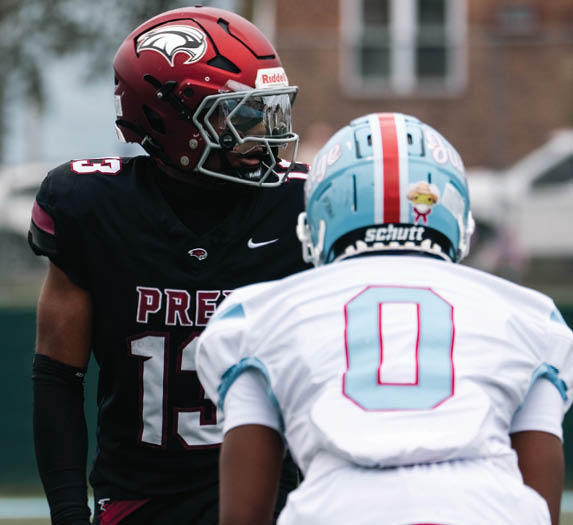 Two people in football uniforms are facing each other on a field, one wearing black with the number 15 and the other wearing white with the number 0. Description generated by AI