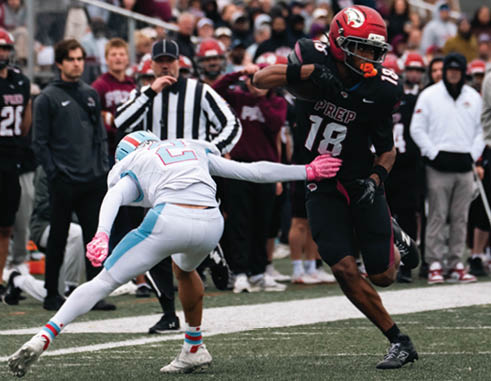 Two people in football uniforms are engaged in a play on a field with one person attempting to tackle the other near the sideline. Description generated by AI