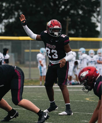 A person wearing a black and maroon football uniform with the number 23 is standing on a field with other players blurred in the background. Description generated by AI