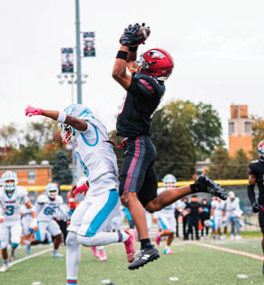 A person wearing a football uniform and helmet is raising one arm in celebration on an outdoor field. Description generated by AI