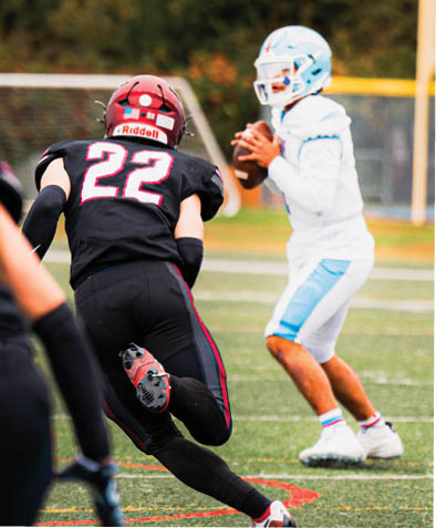 A person wearing a black football uniform with the number 22 is running on a field while another person in a white and blue uniform prepares to throw a football. Description generated by AI