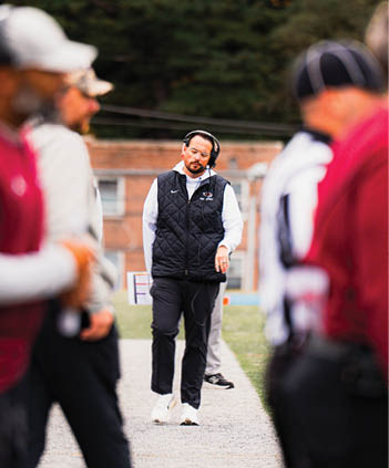 A person wearing headphones and a black quilted vest walks on a path between blurred people in sports attire. Description generated by AI