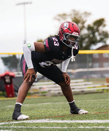 A person wearing a football uniform with the number 23 is in a crouched stance on a grassy field. Description generated by AI