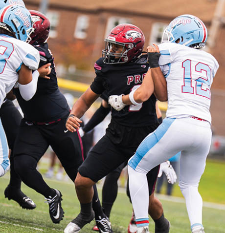 A person wearing a black football uniform with the word PREP and the number 74 on the jersey is sitting on a bench with a red helmet and black faceguard. Description generated by AI
