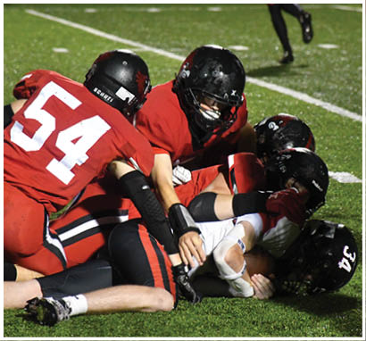 A group of people wearing football uniforms are on a field with one person in a white and green uniform standing in the center and others in red uniforms around them. Description generated by AI