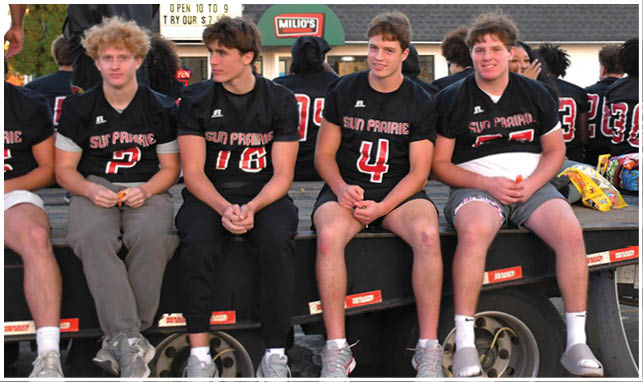 A group of people wearing football uniforms are on a field with one person in a white and green uniform standing in the center and others in red uniforms around them. Description generated by AI