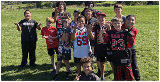A group of people wearing football uniforms are on a field with one person in a white and green uniform standing in the center and others in red uniforms around them. Description generated by AI