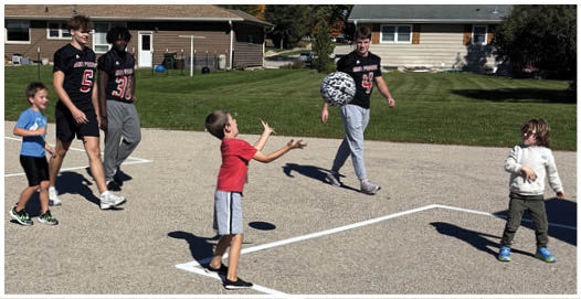 A group of people wearing football uniforms are on a field with one person in a white and green uniform standing in the center and others in red uniforms around them. Description generated by AI