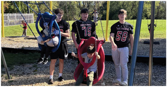 A group of people wearing football uniforms are on a field with one person in a white and green uniform standing in the center and others in red uniforms around them. Description generated by AI