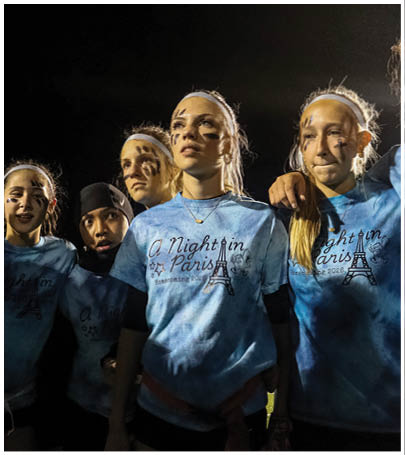 A group of people wearing football uniforms are on a field with one person in a white and green uniform standing in the center and others in red uniforms around them. Description generated by AI