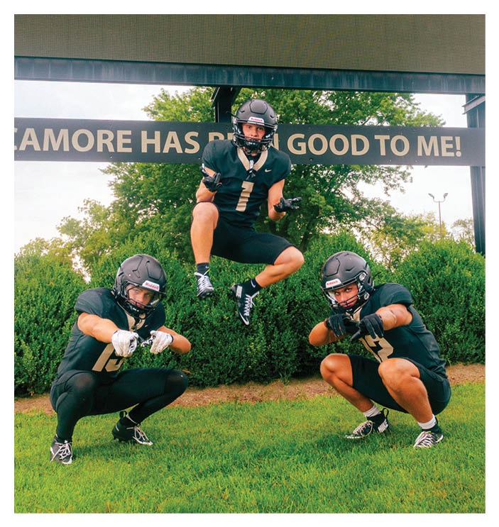 A football game is in progress with players on the field. One player is throwing a football while another player is trying to catch it. The players are wearing uniforms and are actively engaged in the game. AI generated content