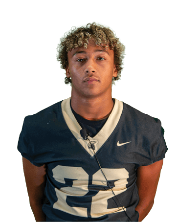 Person with curly hair wearing a dark sports jersey with a microphone clipped to the collar against a white background. Description generated by AI