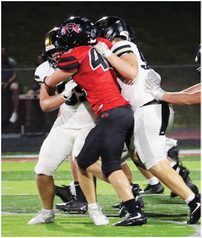 Several people in football uniforms are engaged in a play on a field under stadium lights. Description generated by AI