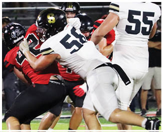 Several people in football uniforms are actively engaged in a play on a well-lit field during a nighttime game. Description generated by AI