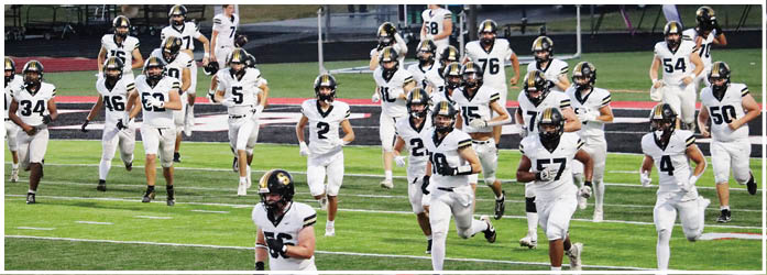 A group of people wearing white football uniforms and helmets are walking on a football field. Description generated by AI