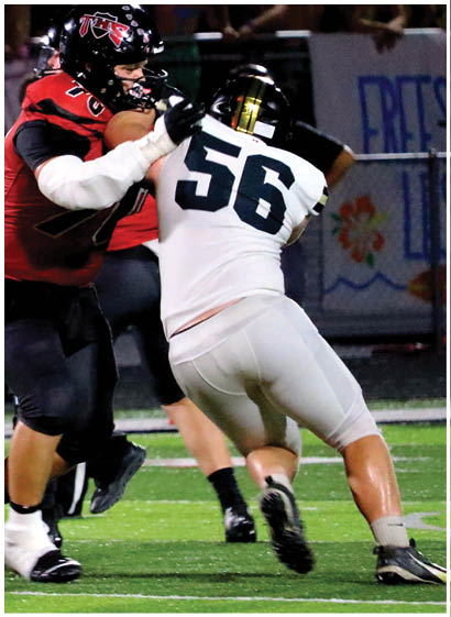 Two people in football uniforms are engaged in a physical play on a field during a game, with one wearing red and black and the other in white and black. Description generated by AI