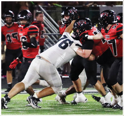 People in football uniforms are engaged in a close physical play on a grassy field during a game. Description generated by AI