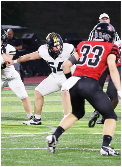 Two people in white football uniforms are engaged in a play on a field while a person in a red and black uniform moves toward them. Description generated by AI