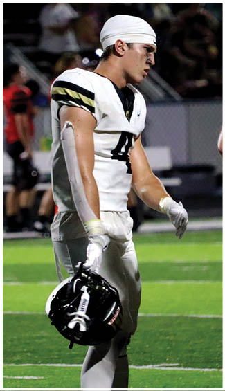 A person wearing a white football uniform and headband stands on a field looking to the side with a focused expression. Description generated by AI