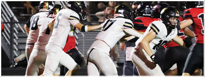 Several people wearing white and black football uniforms are running on a field while others in red and black uniforms are nearby. Description generated by AI
