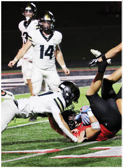 A person in a white sports uniform is diving to tackle another person in a black and red uniform who is falling backward on a football field. Description generated by AI