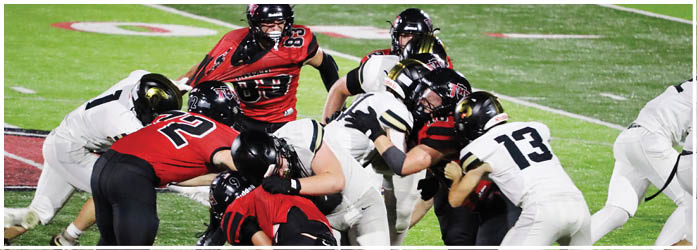 People wearing red and white football uniforms are engaged in a tackle on a green field during a game. Description generated by AI