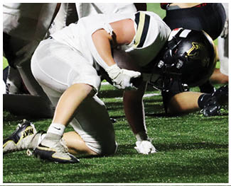 Two people in football gear are positioned on a field, one holding a football and the other wearing a helmet with a logo. Description generated by AI