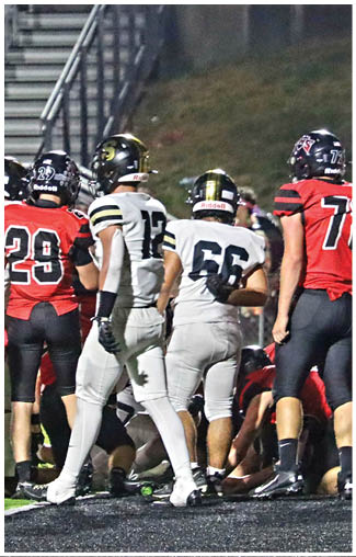 People wearing football uniforms are standing and crouching on a field during a nighttime game. Description generated by AI