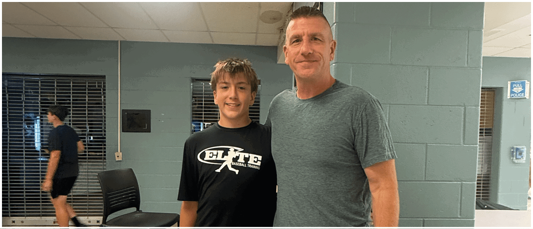 Two adults wearing casual athletic clothing stand indoors near a trash can and a wall with a door and chair in the background. Description generated by AI