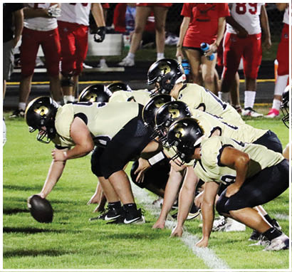 A group of football players in black and gold uniforms are lined up on the field in a crouched position ready for a play during a game. Description generated by AI